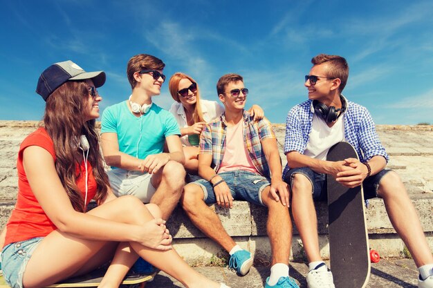 vriendschap, vrije tijd, zomer en mensenconcept - groep glimlachende vrienden met skateboards die op stadsstraat zitten