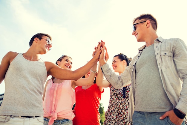 vriendschap, vrije tijd, zomer, gebaren en mensen concept - groep lachende vrienden die high five buitenshuis maken