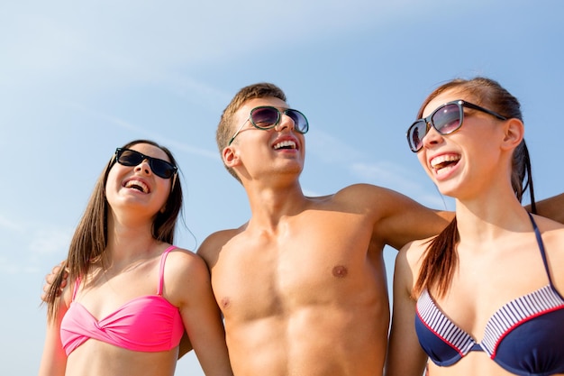 vriendschap, zee, zomervakantie, vakantie en mensen concept - groep lachende vrienden die badkleding en zonnebril dragen die op het strand praten