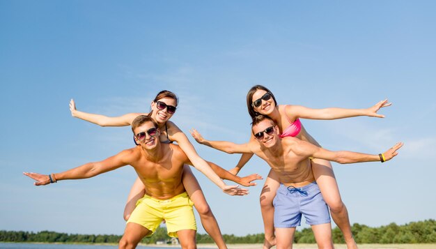 vriendschap, zee, zomervakantie, vakantie en mensen concept - groep lachende vrienden die badkleding en zonnebril dragen die plezier hebben op het strand