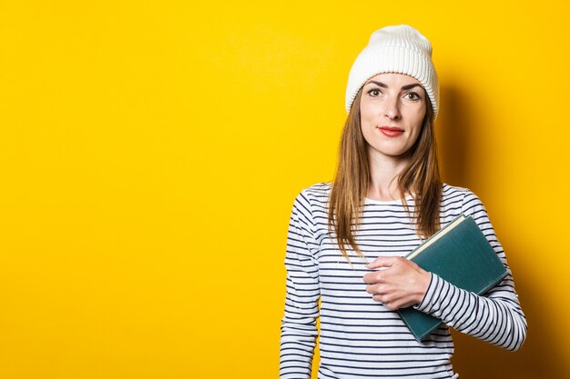 Vriendschappelijke jonge vrouw die een boek op een gele achtergrond houdt