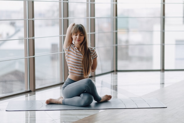 Vrij aantrekkelijk meisje dat yoga doet en in de heldere ruimte ontspant