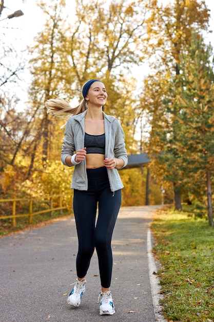 Vrij atletische vrouw draait op zonnige herfstdag, geniet van het joggen. aport en welzijnsconcept