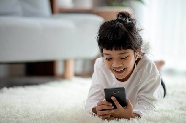 Vrij Aziatisch meisje dat een koptelefoon gebruikt om naar muziek te luisteren via een smartphone in de woonkamer