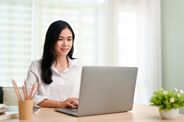 Vrij Aziatische zakenvrouw die aan haar taken op laptop op kantoor werkt