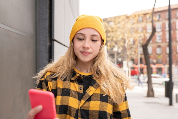 Vrij blanke vrouw met gele hoed en overhemd, met smartphone in de straat