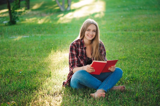 Vrij blonde jonge vrouw die een boek leest bij park