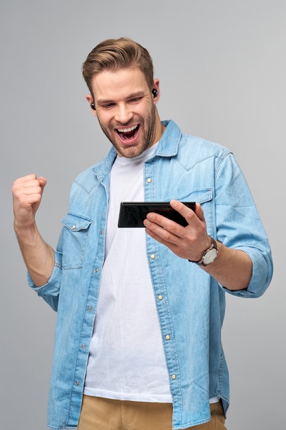 vrij casual man in spijkerbroek shirt met zijn telefoon staande over studio grijze muur