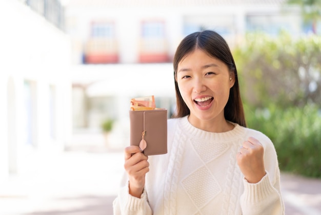 Vrij chinese vrouw die buiten portemonnee met geld vasthoudt en een overwinning viert