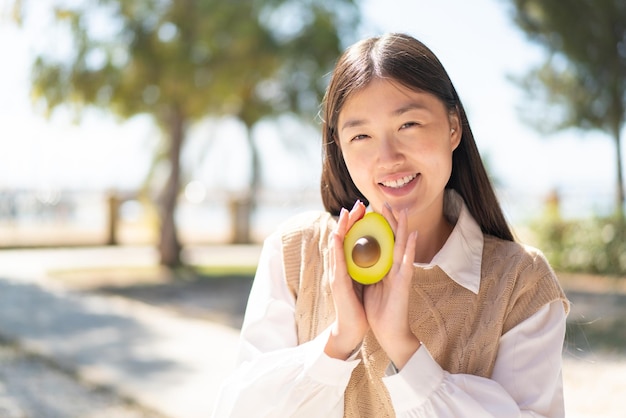 Vrij Chinese vrouw die in openlucht een avocado met gelukkige uitdrukking houdt