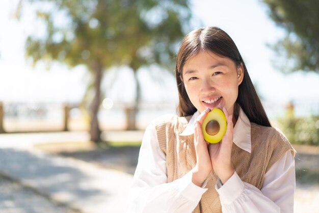 Vrij chinese vrouw die in openlucht een avocado met gelukkige uitdrukking houdt