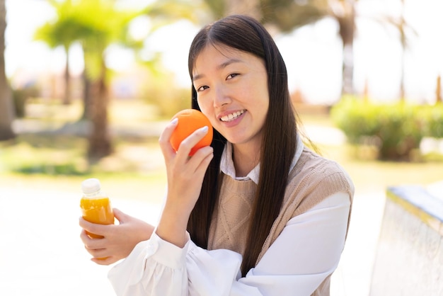 Vrij Chinese vrouw die in openlucht een sinaasappel en een jus d'orange houdt
