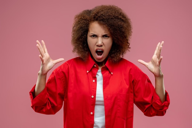 Vrij curlyhaired vrouw die in rood jasje boos kijkt