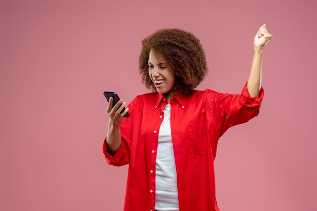 Vrij curlyhaired vrouw in rode jas die er gelukkig uitziet