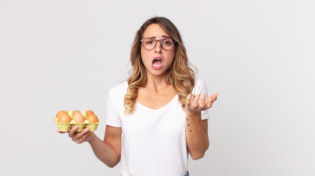 Vrij dunne vrouw die er wanhopig, gefrustreerd en gestrest uitziet en een eierdoos vasthoudt