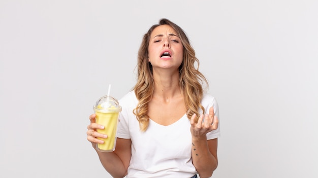 Vrij dunne vrouw die er wanhopig, gefrustreerd en gestrest uitziet en een vanillemilkshake vasthoudt