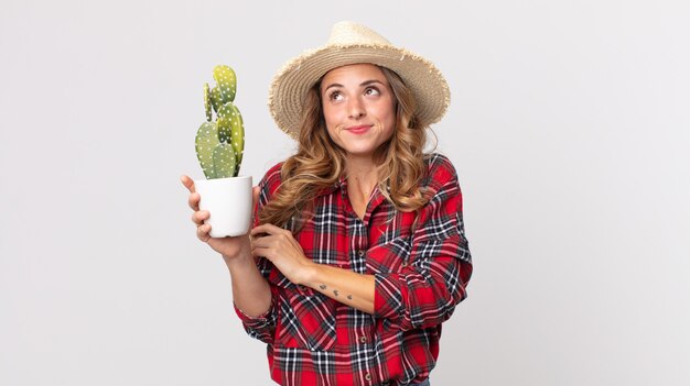 Vrij dunne vrouw die haar schouders ophaalt, zich verward en onzeker voelt en een cactus vasthoudt. boer concept