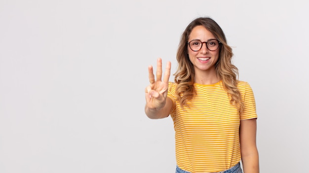 Vrij dunne vrouw die lacht en er vriendelijk uitziet, nummer drie of derde toont met de hand naar voren, aftellend