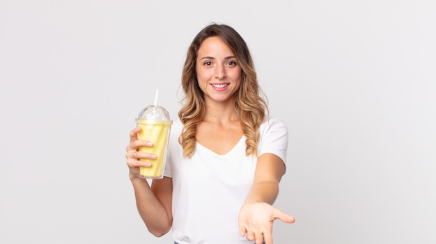 Vrij dunne vrouw die vrolijk lacht met vriendelijk en een concept aanbiedt en toont en een vanillemilkshake vasthoudt