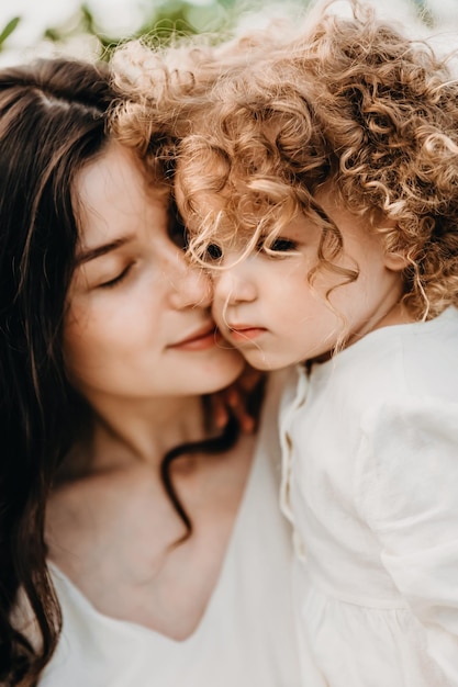 Vrij gekrulde dochter loopt met moeder in het zonnige park Het concept van zomervakantie buitenshuis Moederdag baby's dag Tijd samen doorbrengen