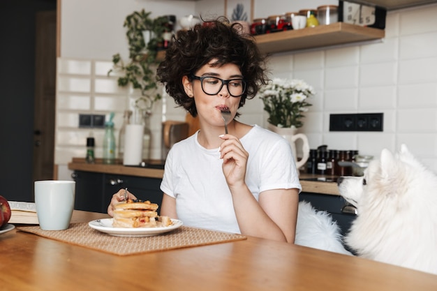 vrij gekrulde vrouw die aan de keuken zit, het drinken van thee, eet cake