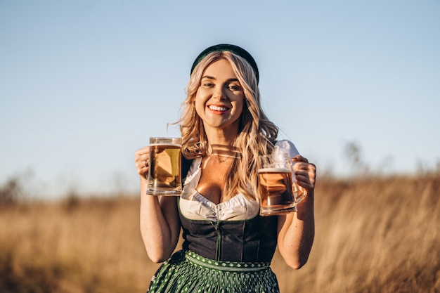Vrij gelukkig blonde in dirndl, traditionele festival jurk, met twee mokken bier buiten in het veld