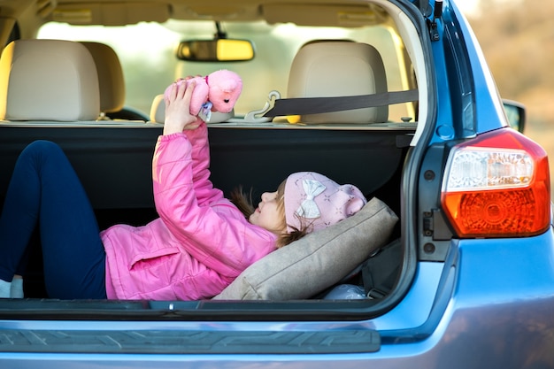 Vrij gelukkig kind meisje speelt met een roze speelgoed teddybeer in een auto kofferbak.