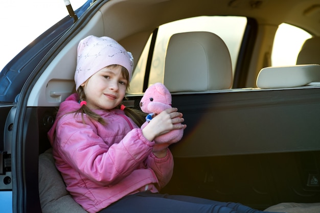 Vrij gelukkig kindmeisje het spelen met een roze stuk speelgoed teddybeerzitting in een autoboomstam.