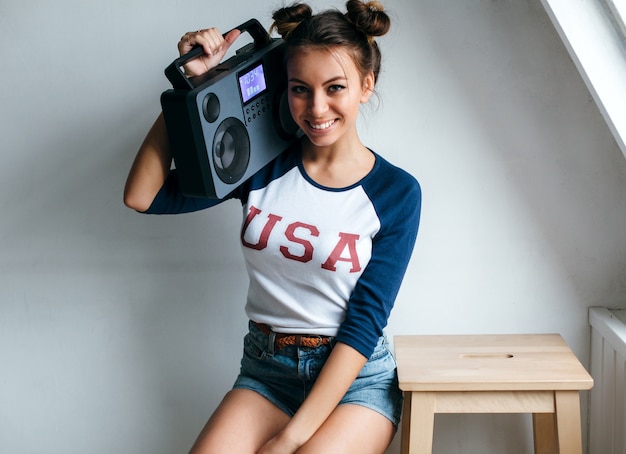 Vrij het jonge sexy gelooide meisje stellen in de zomer in witte studio met hifi moderne bandrecorder