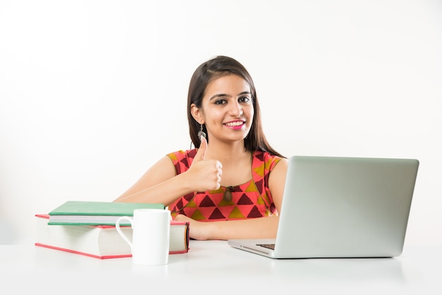 Vrij Indiase Aziatische meisje studeren op laptopcomputer met stapel boeken op tafel, op witte achtergrond