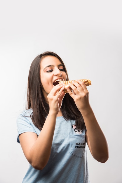 Vrij Indisch Aziatisch jong meisje dat gegrilde sandwich eet, geïsoleerd over gele of witte achtergrond