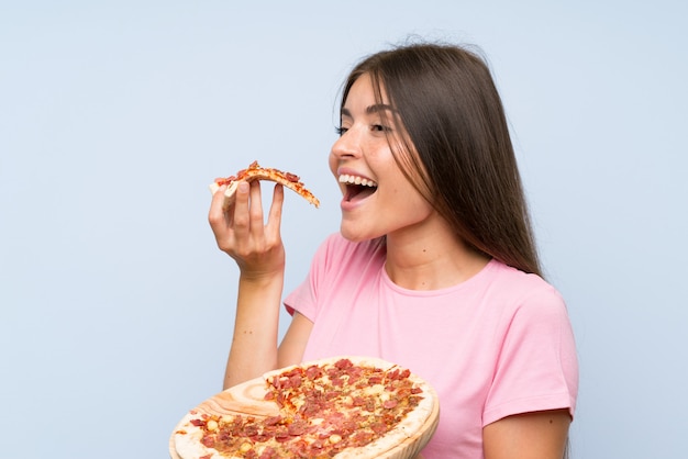 Vrij jong meisje dat een pizza over geïsoleerde blauwe muur houdt