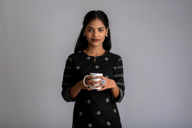 Vrij jong meisje met een kopje thee of koffie die zich voordeed op een grijze achtergrond