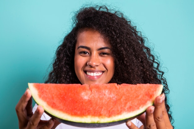 Vrij jong meisje met plakje watermeloen voor haar gezicht. Portret van glimlachend Afrikaans Amerikaans meisje geïsoleerd