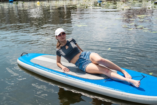 Vrij jong slank vrouwelijk model liggend op sup board op zonnige ochtend op oceaan strand levensstijl gezondheid en ontspannen