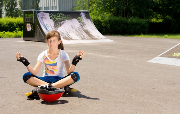 Vrij jong tienermeisje in rollerblades zitten mediteren op het asfalt
