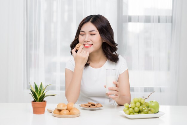 Vrij jonge Aziatische vrouw die smakelijk koekje thuis eet.