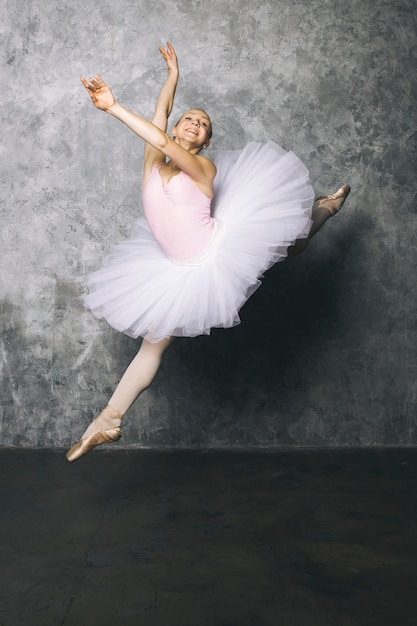 Vrij jonge ballerinadanser die klassiek ballet dansen tegen rustieke muur