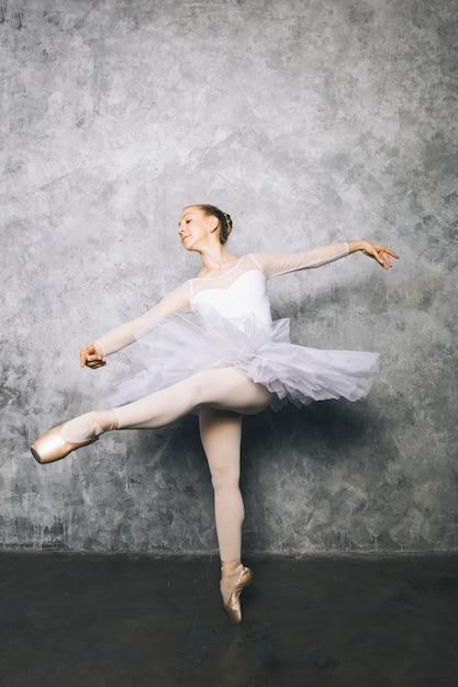 Vrij jonge ballerinadanser die klassiek ballet dansen tegen rustieke muur