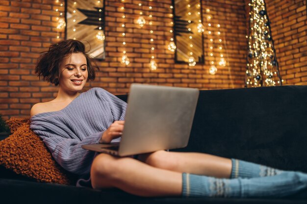 Vrij jonge brunette thuis op de bank met laptop