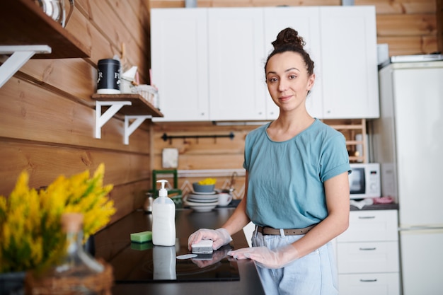 Vrij jonge huisvrouw met spons die zich door elektrisch fornuis in de keuken bevindt tijdens het schoonmaken