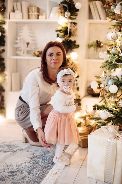 Vrij jonge moeder en haar dochtertje die naast een kerstboom in hun huis blijven. Kerst vakantie concept