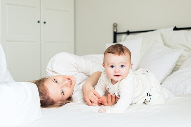 Vrij jonge moeder met haar zoontje in bed. Grappige lachende ochtend. witte slaapkamer