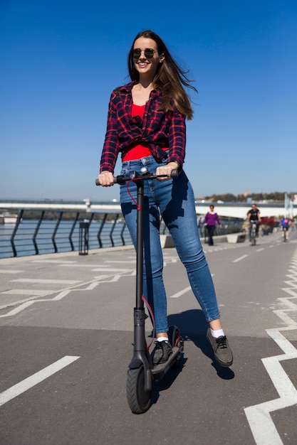 Vrij jonge vrouw die een elektrische autoped in de straat berijdt