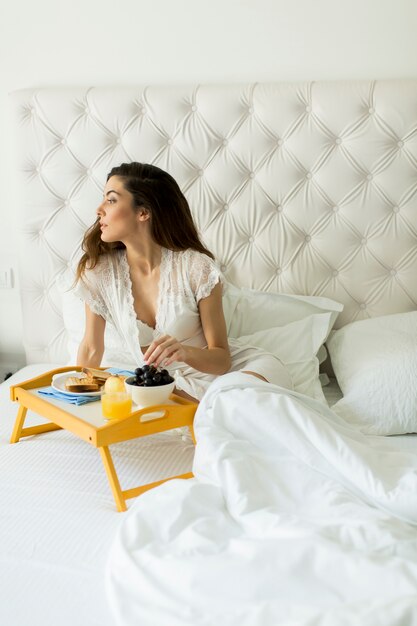 Vrij jonge vrouw die een ontbijt in het bed heeft