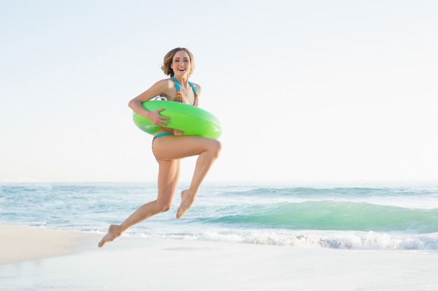 Vrij jonge vrouw die een rubberring houdt terwijl het springen op strand