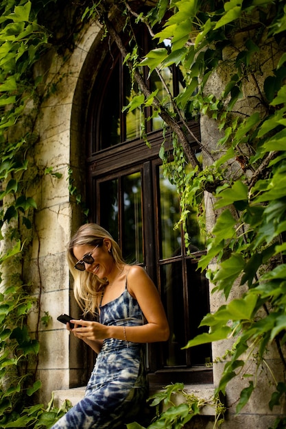 Vrij jonge vrouw die mobiele telefoon gebruikt door oud huis met klimop