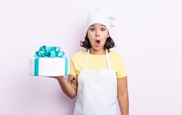 Vrij jonge vrouw die zeer geschokt of verrast kijkt. chef-kok die een cake kookt