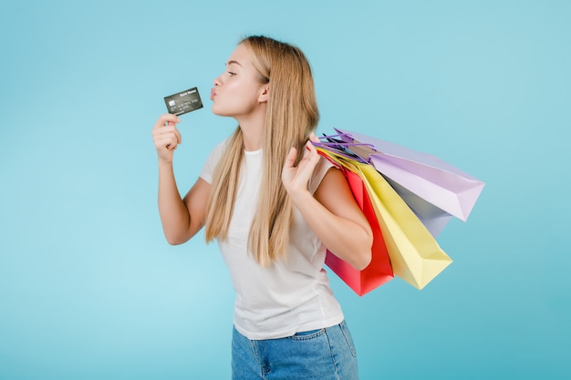 Vrij jonge vrouw met creditcard en kleurrijke die het winkelen zakken over blauw wordt geïsoleerd