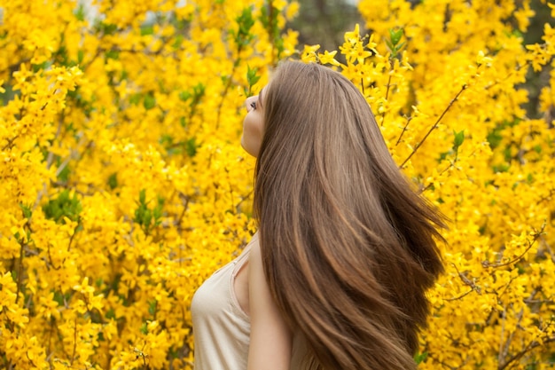 Vrij jonge vrouw met lang waaiend haar op bloemenachtergrond buiten